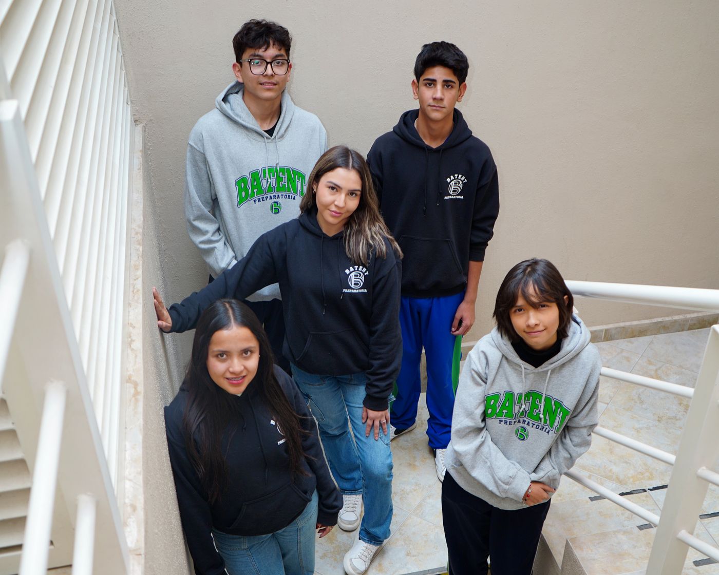 Cinco alumnos de BATENT con sudaderas de la preparatoria posando en las escaleras de la escuela