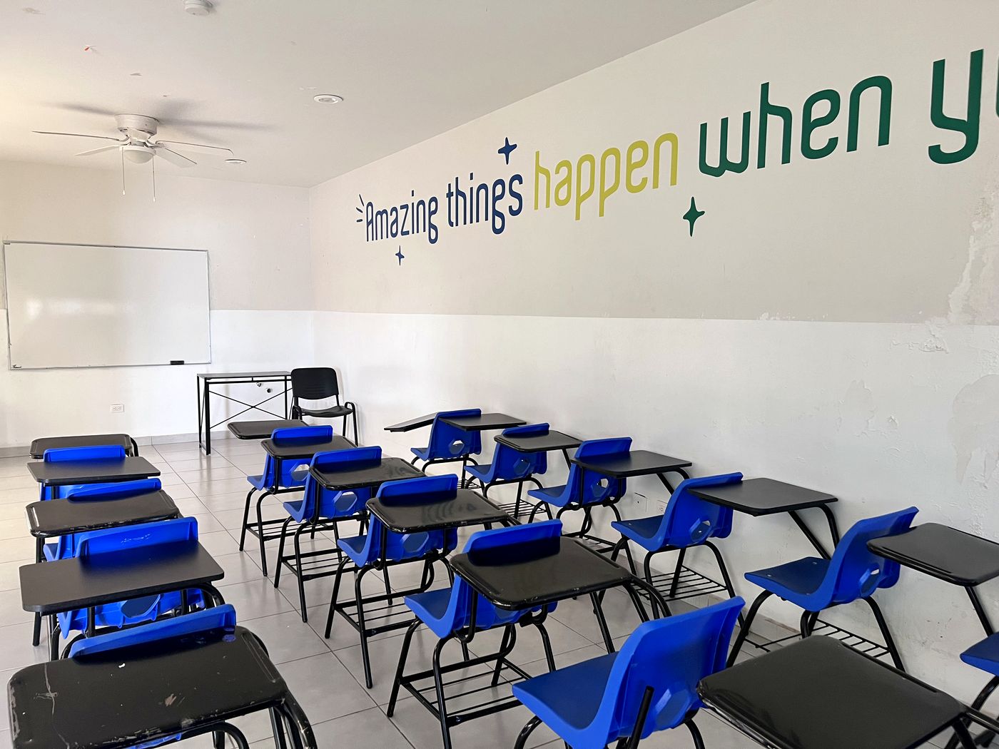Salón de clases con pupitres azules y pizarrón